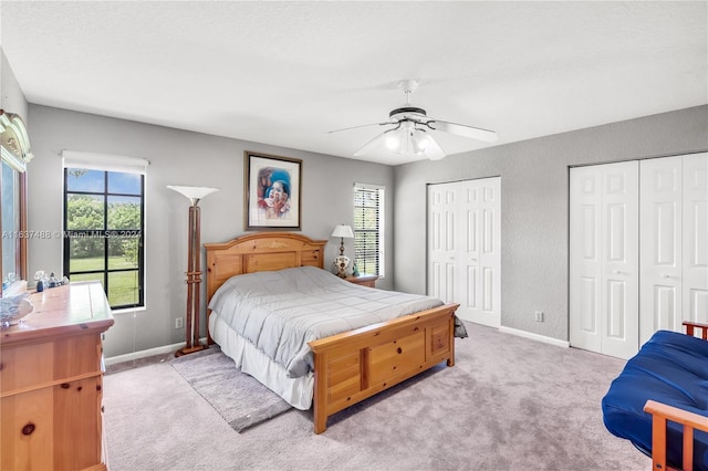 bedroom featuring multiple windows, ceiling fan, light colored carpet, and two closets