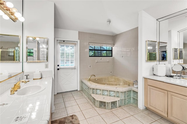 bathroom with tile patterned flooring, vanity, and a relaxing tiled tub