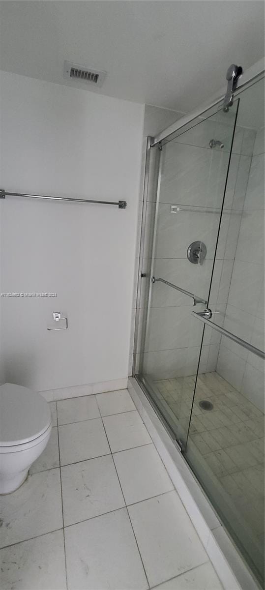 bathroom featuring a shower with door, toilet, and tile patterned floors