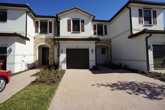 view of front facade with stucco siding, stone siding, a garage, and decorative driveway