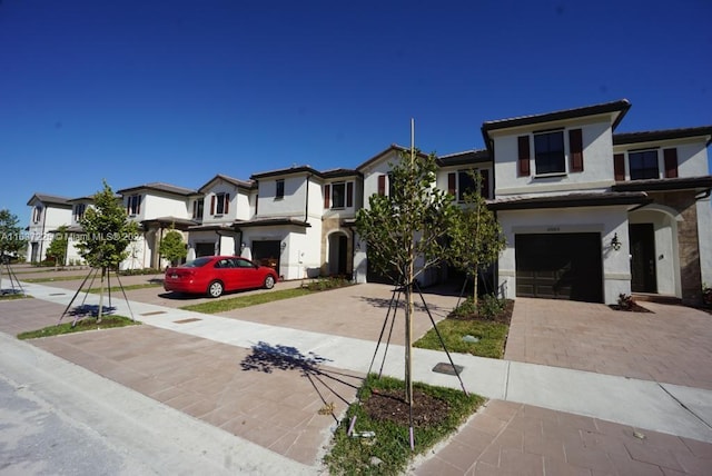 view of front of house with decorative driveway, a residential view, an attached garage, and stucco siding