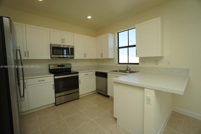 kitchen with light countertops, appliances with stainless steel finishes, a peninsula, white cabinetry, and a sink