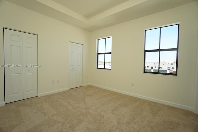 unfurnished bedroom with a tray ceiling, baseboards, and light carpet