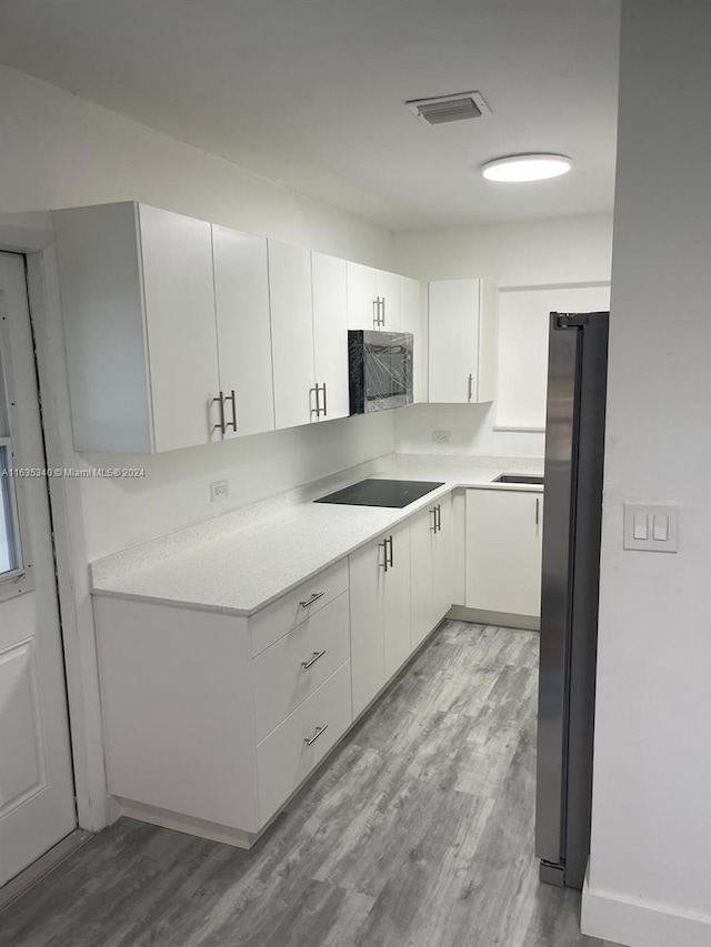 kitchen with black electric cooktop, white cabinetry, fridge, and light hardwood / wood-style flooring