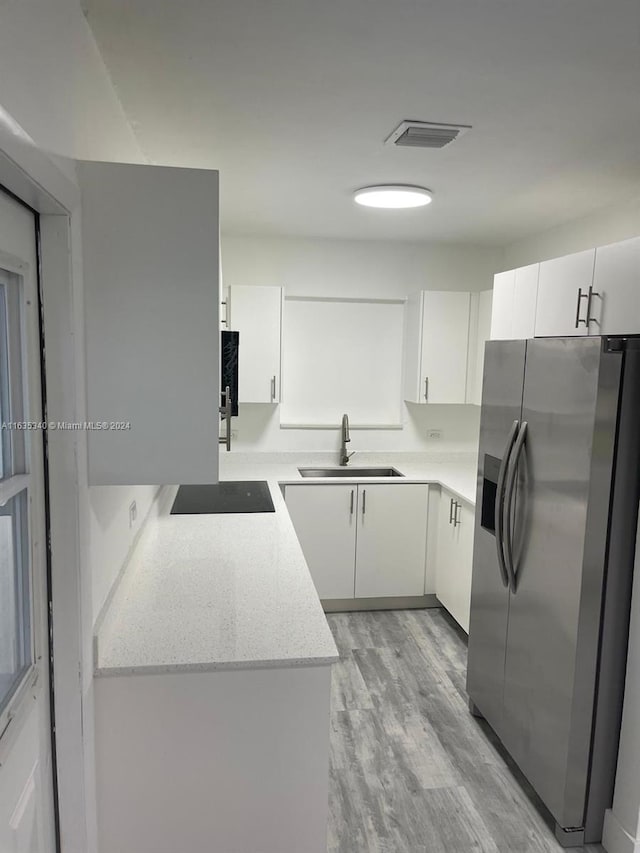 kitchen with stainless steel fridge with ice dispenser, white cabinetry, light hardwood / wood-style flooring, electric stovetop, and sink