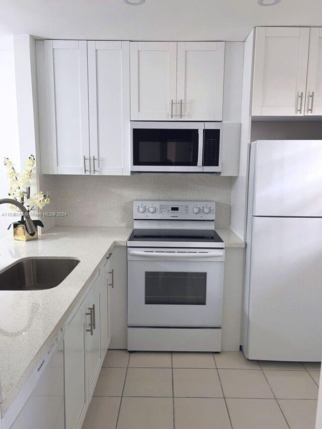 kitchen with white appliances, white cabinets, sink, light stone countertops, and light tile patterned flooring