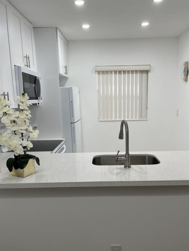 kitchen featuring sink, white fridge, white cabinets, and light stone countertops