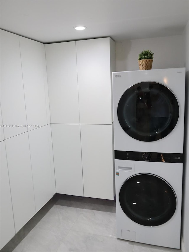 laundry room with light tile patterned flooring, cabinets, and stacked washer / dryer