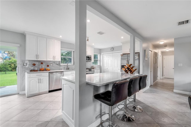 kitchen featuring a kitchen bar, stainless steel appliances, white cabinets, decorative backsplash, and light tile patterned floors