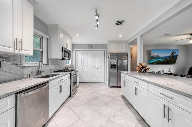 kitchen featuring appliances with stainless steel finishes, white cabinetry, light stone countertops, and sink