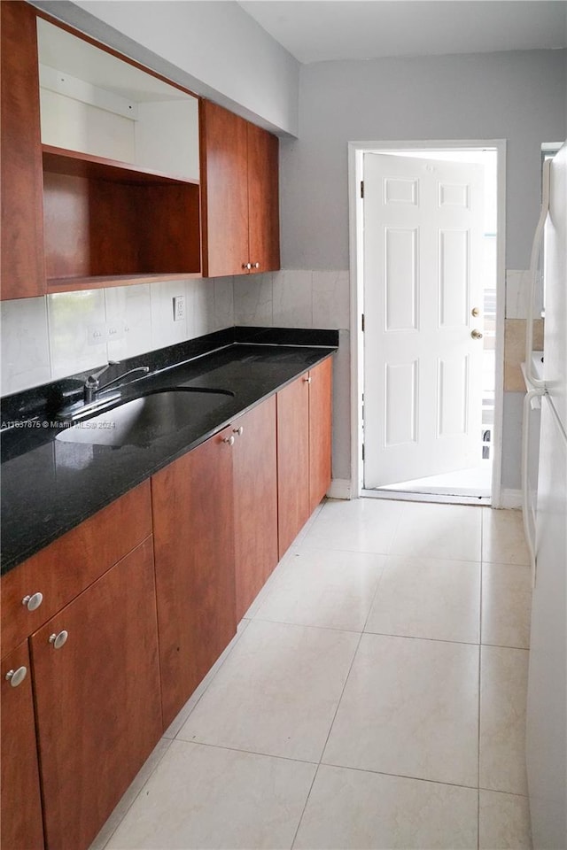 kitchen featuring light tile patterned flooring, white refrigerator, tasteful backsplash, sink, and dark stone countertops