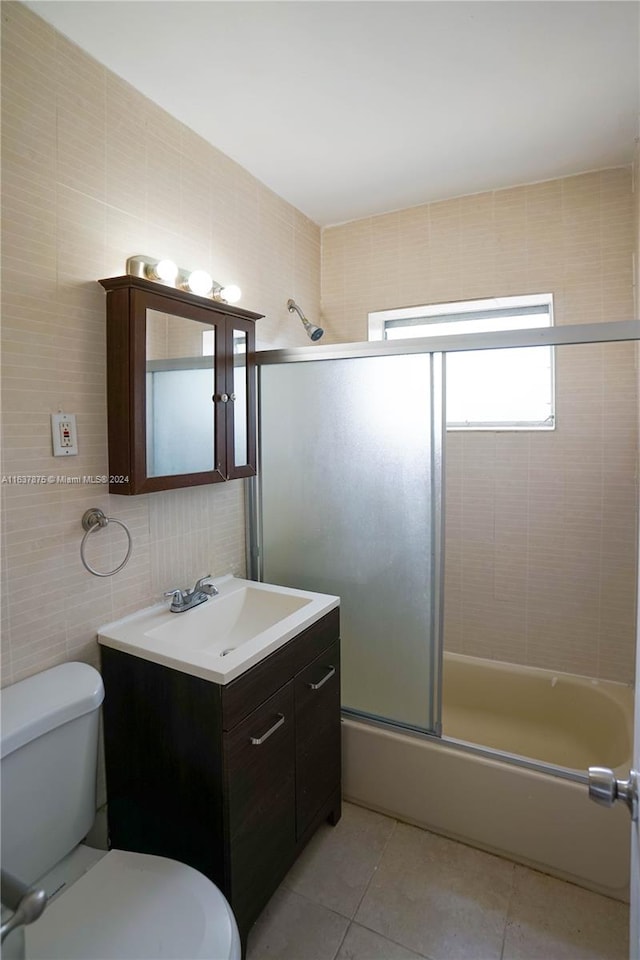 full bathroom featuring tile walls, shower / bath combination with glass door, tile patterned floors, toilet, and vanity