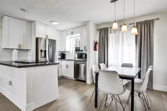 kitchen with appliances with stainless steel finishes, light hardwood / wood-style flooring, sink, hanging light fixtures, and white cabinetry