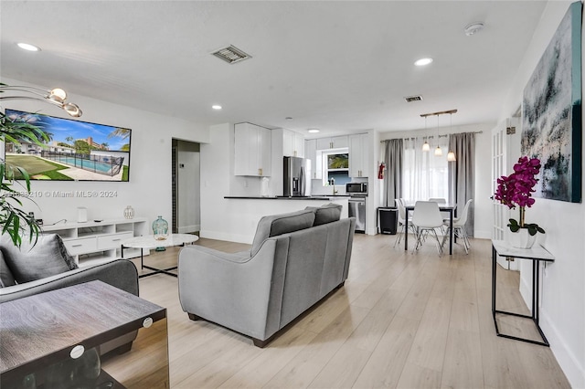 living room featuring sink, light hardwood / wood-style flooring, and a notable chandelier