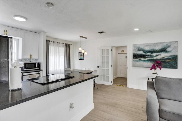 kitchen with dark stone counters, decorative light fixtures, light wood-type flooring, white cabinetry, and black cooktop