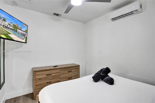 bedroom featuring hardwood / wood-style flooring, a wall mounted air conditioner, and ceiling fan