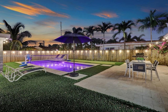 pool at dusk featuring a patio and a lawn