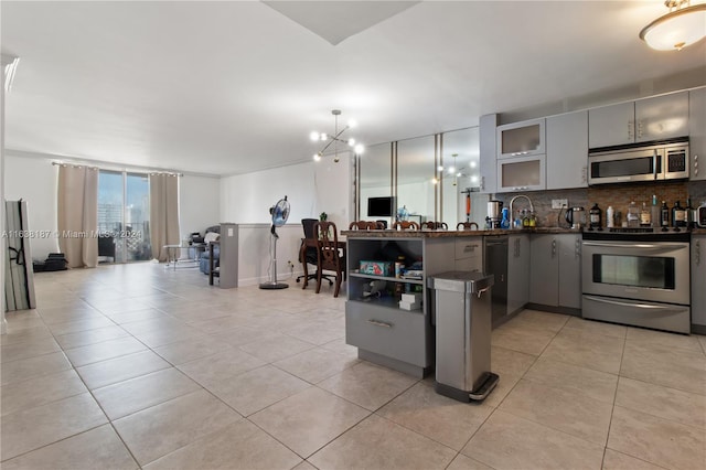 kitchen featuring gray cabinets, stainless steel appliances, a chandelier, and tasteful backsplash