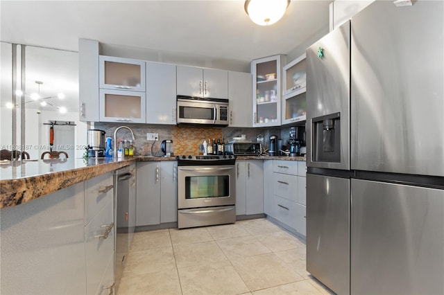 kitchen featuring stainless steel appliances, backsplash, light tile patterned floors, and gray cabinetry