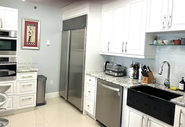 kitchen with light tile patterned floors, appliances with stainless steel finishes, light stone countertops, tasteful backsplash, and white cabinetry