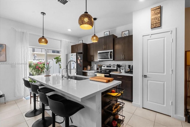 kitchen with sink, appliances with stainless steel finishes, a kitchen island with sink, and light tile patterned floors