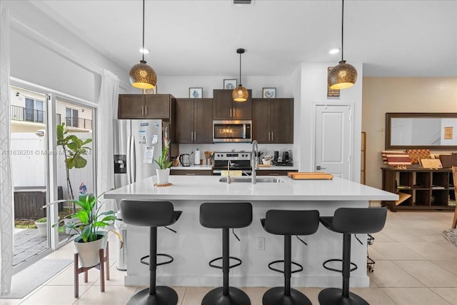 kitchen featuring light tile patterned floors, stainless steel appliances, hanging light fixtures, sink, and a center island with sink