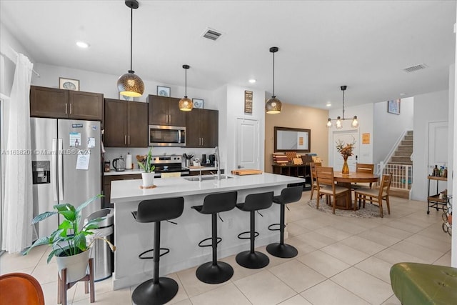 kitchen featuring stainless steel appliances, sink, pendant lighting, dark brown cabinetry, and light tile patterned flooring