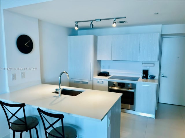 kitchen with black electric cooktop, oven, a peninsula, a sink, and a breakfast bar area