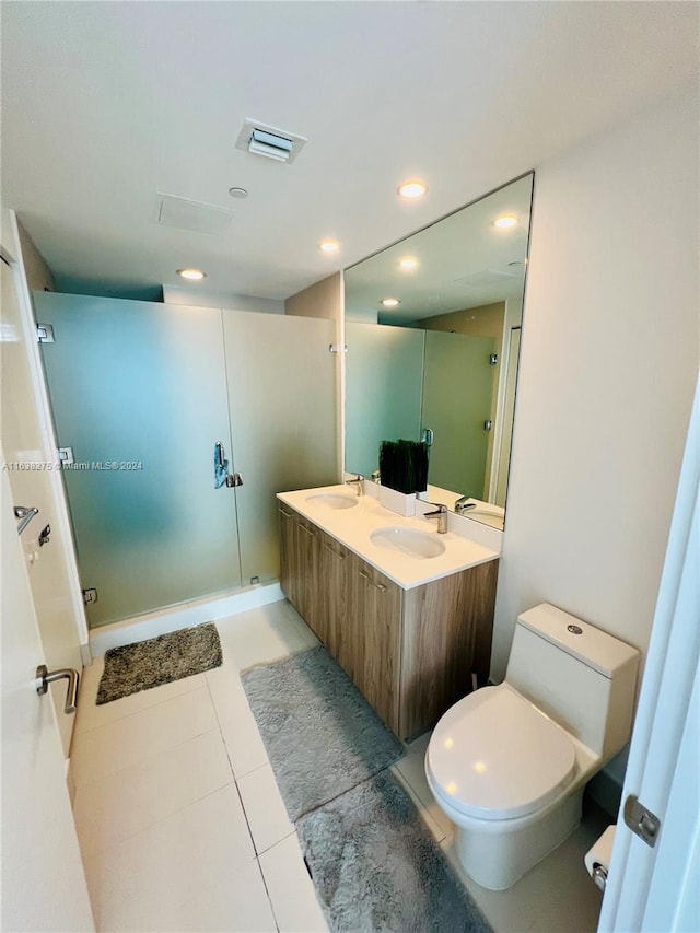 bathroom featuring a shower with shower door, dual bowl vanity, toilet, and tile patterned floors