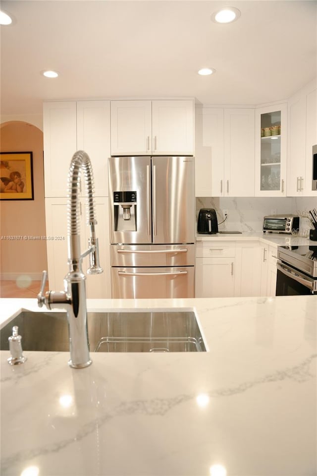 kitchen featuring stainless steel fridge with ice dispenser, tasteful backsplash, white cabinets, light stone countertops, and stove