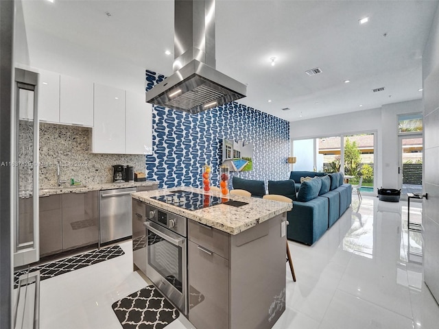 kitchen with stainless steel appliances, a center island, light stone counters, island range hood, and white cabinets