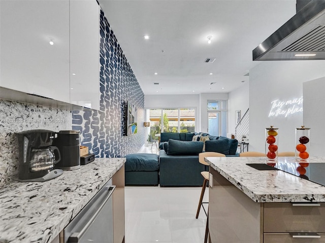 kitchen with a kitchen island, custom range hood, light stone counters, and a kitchen breakfast bar