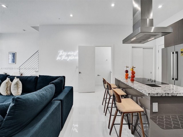 kitchen with a kitchen bar, island exhaust hood, light stone countertops, high end fridge, and black electric cooktop