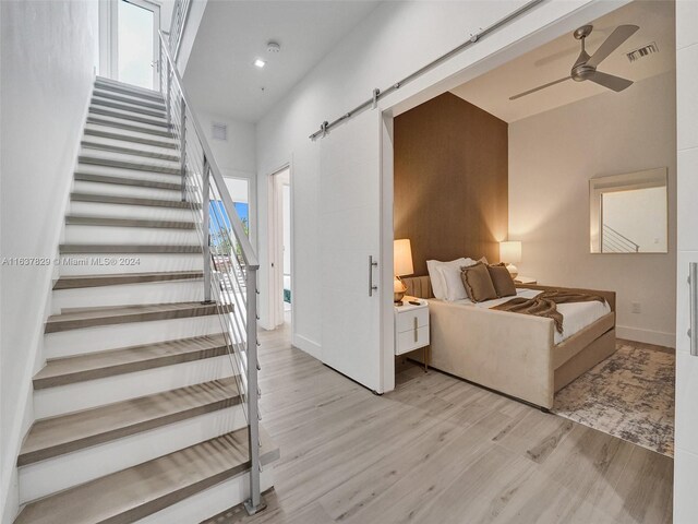 staircase featuring hardwood / wood-style flooring, ceiling fan, a healthy amount of sunlight, and a barn door