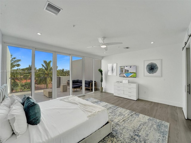 bedroom with wood-type flooring, a barn door, and ceiling fan