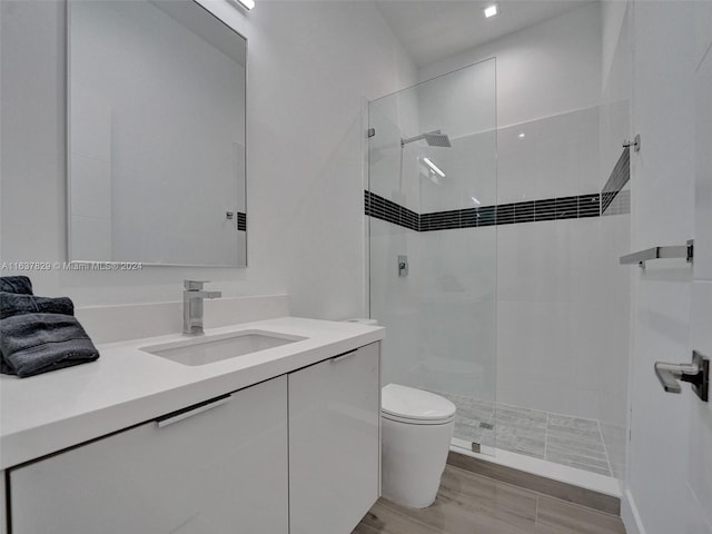 bathroom with vanity, toilet, wood-type flooring, and a tile shower