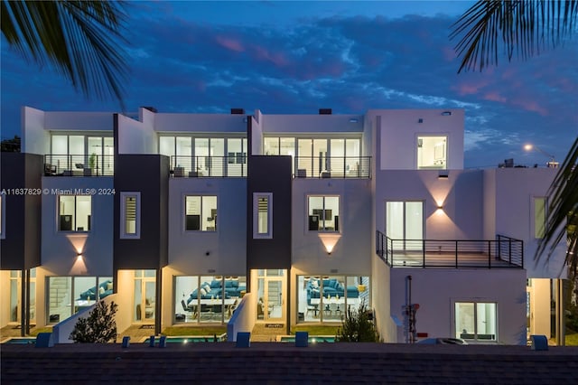 back house at dusk featuring a balcony