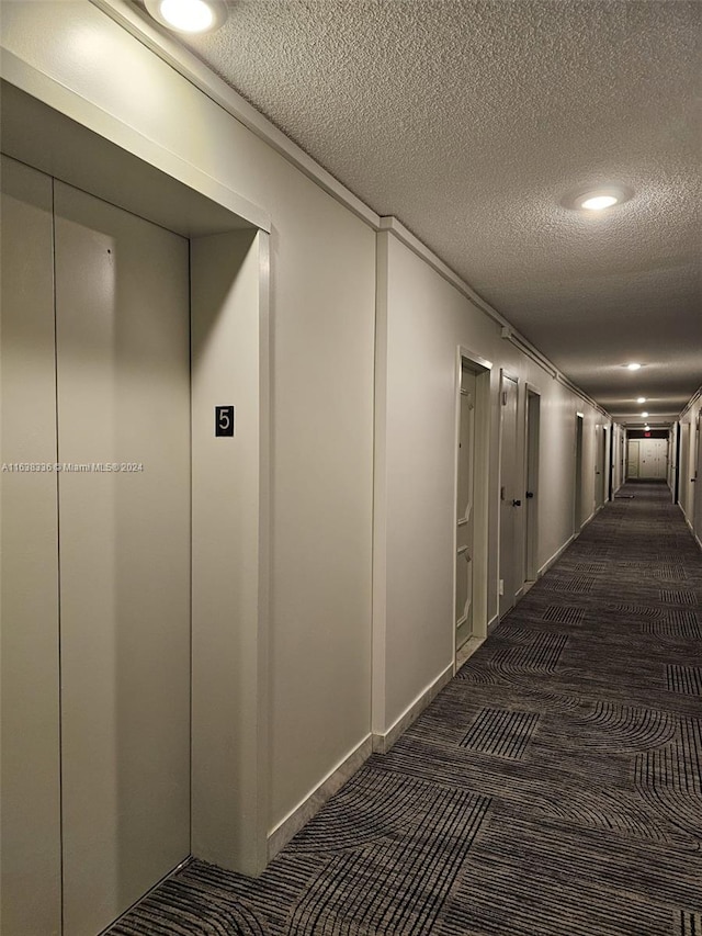 hall with elevator, a textured ceiling, and dark carpet