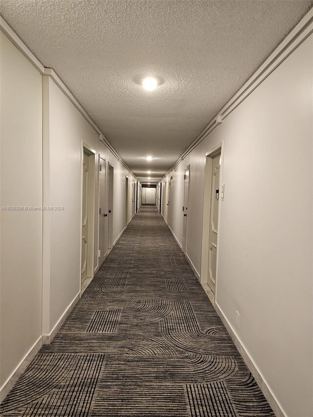 hallway with dark colored carpet, a textured ceiling, and crown molding