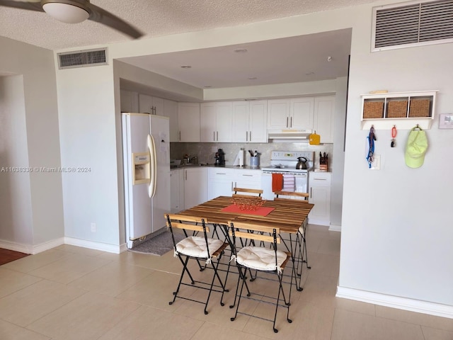 kitchen with white appliances, a textured ceiling, light tile patterned floors, and white cabinets