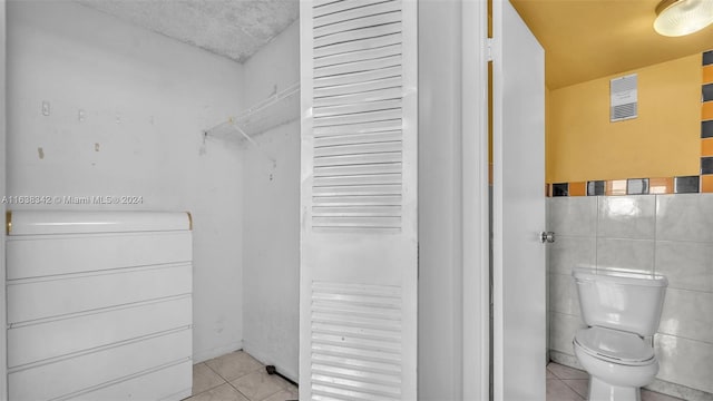 bathroom with toilet, tile patterned floors, and tile walls