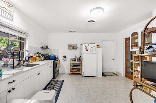 kitchen with light tile patterned flooring, white refrigerator, stainless steel electric stove, white cabinets, and sink