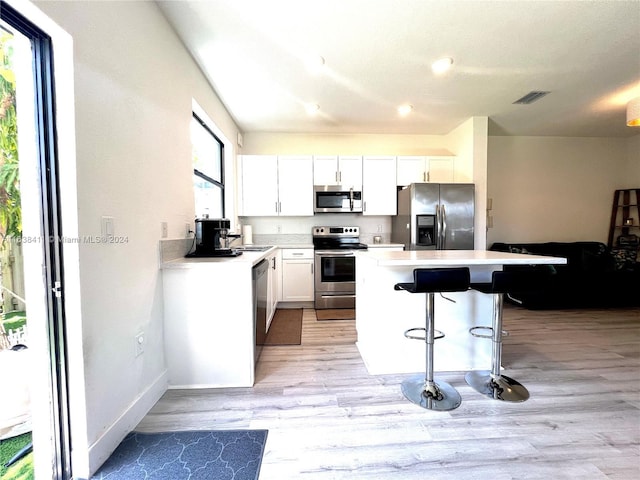 kitchen with a breakfast bar area, light hardwood / wood-style flooring, white cabinetry, stainless steel appliances, and a kitchen island