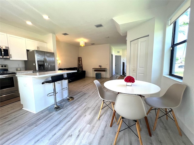 kitchen with light hardwood / wood-style flooring, appliances with stainless steel finishes, white cabinetry, a kitchen breakfast bar, and a center island