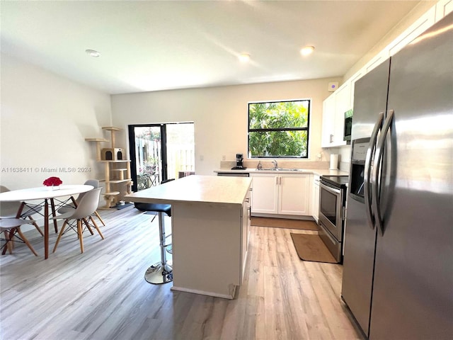 kitchen featuring sink, appliances with stainless steel finishes, white cabinetry, a kitchen island, and a kitchen bar