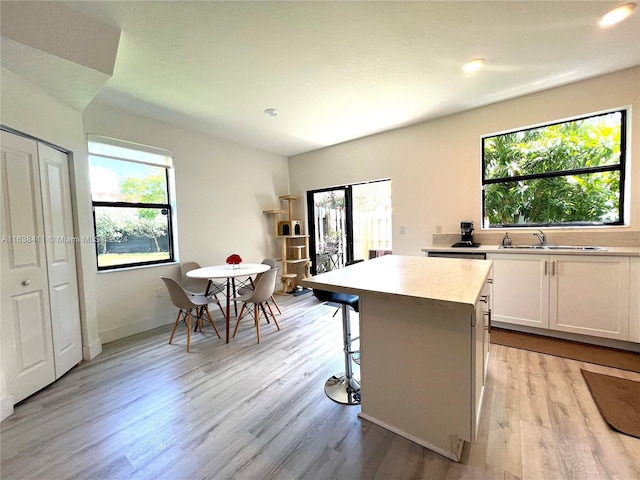 kitchen featuring sink, a center island, light hardwood / wood-style floors, white cabinets, and a kitchen bar