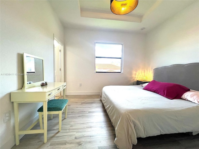 bedroom with a raised ceiling and light wood-type flooring