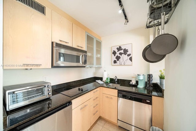 kitchen with appliances with stainless steel finishes, track lighting, dark stone countertops, light tile patterned floors, and light brown cabinetry