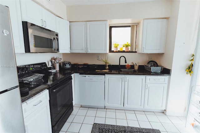 kitchen with dark stone counters, white appliances, sink, light tile patterned floors, and white cabinetry