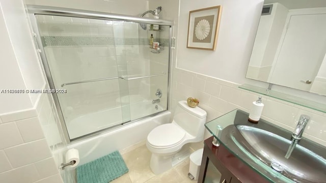 full bathroom featuring tile patterned flooring, bath / shower combo with glass door, tasteful backsplash, toilet, and tile walls